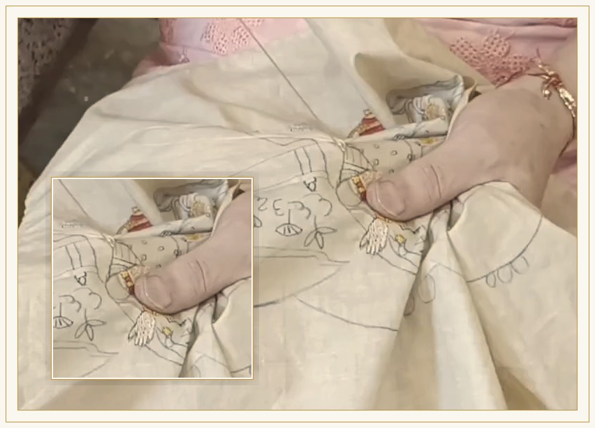 A needle and silk thread at work on cloth held in the hand